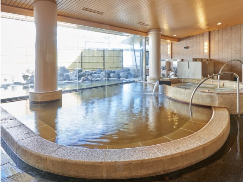 【14F 大浴場　天-TEN-】
ホテル最上階に位置する天然温泉が湧き出る大浴場。野趣あふれる露天風呂や、源泉掛け流しのかめ湯やサウナ、そしてロビーにはマッサージチェアも併設され、温泉旅館さながらのくつろぎをご体感いただけます。