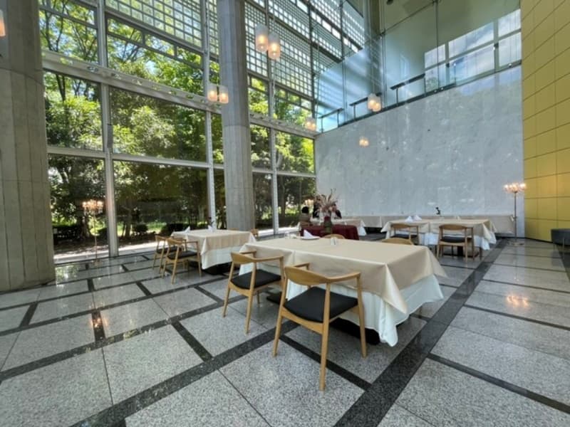 天井まで広がるガラス張りの開放的な会場全景。緑を望む明るい空間は、立食・着席どちらのスタイルにも対応し、華やかなパーティーシーンを引き立てます。（着席は50名様迄です。）