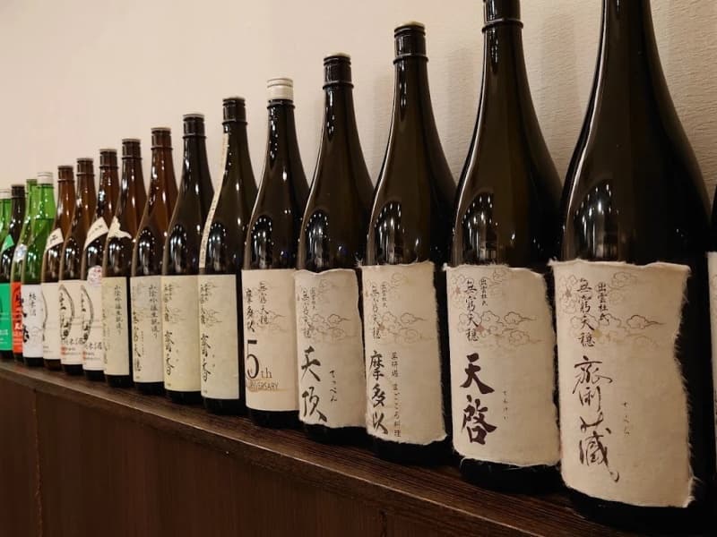 壁面に整然と並ぶ厳選日本酒のボトル。蔵元から丁寧に選び抜いた純米酒が、旬の料理との絶妙なペアリングを演出します。