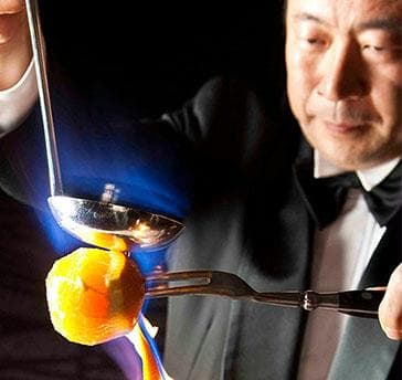 【カフェレジェンド】
音楽に合わせて剥いたオレンジの皮を、ラム酒やオレンジキュラソーでフランベ。甘い香りと青い炎が幻想的に会場を包みます。パフォーマンス後には皆さまにオレンジリキュール香る甘いコーヒーを楽しんでいただきます。