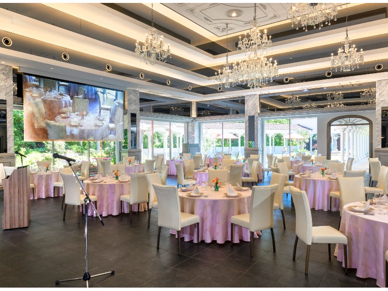 大きな窓の向こうにガーデンが拡がる。華やかなシャンデリアが煌めくパーティ会場
