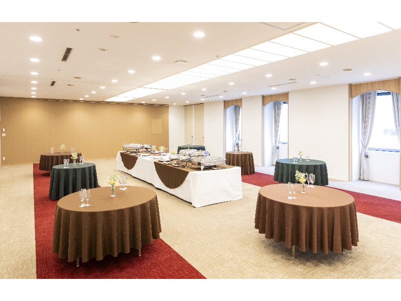 窓から自然光が差し込む明るい会場「結」は、落ち着いた色調のインテリアと温かみのある照明で、和やかな雰囲気を演出します。白を基調とした壁とベージュのカーペットが上品な印象を与え、ビジネスからパーティまで多目的にご利用いただけます。