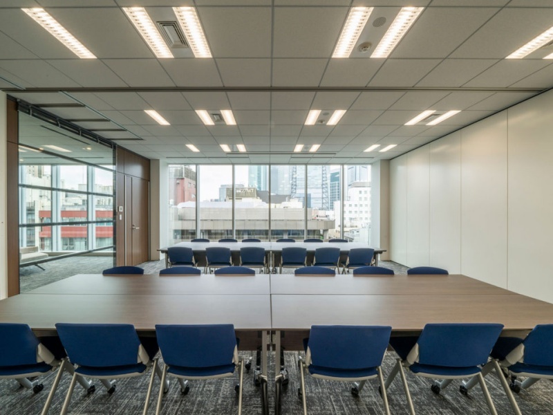 柱のないフラットな連結空間です。廊下側の全面ガラスウォールが室内の奥行きを引き立て、白を基調とした内装とブルーのチェアが清潔感を際立たせています。遮るもののない広々とした視界が、質の高いミーティング環境を提供します。