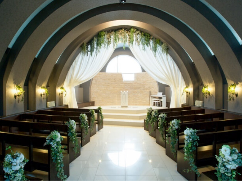 アーチ状の天井と緑の装飾が美しいチャペル。白いドレープカーテンから差し込む柔らかな光が、厳かで温かな空間を作り出しています。