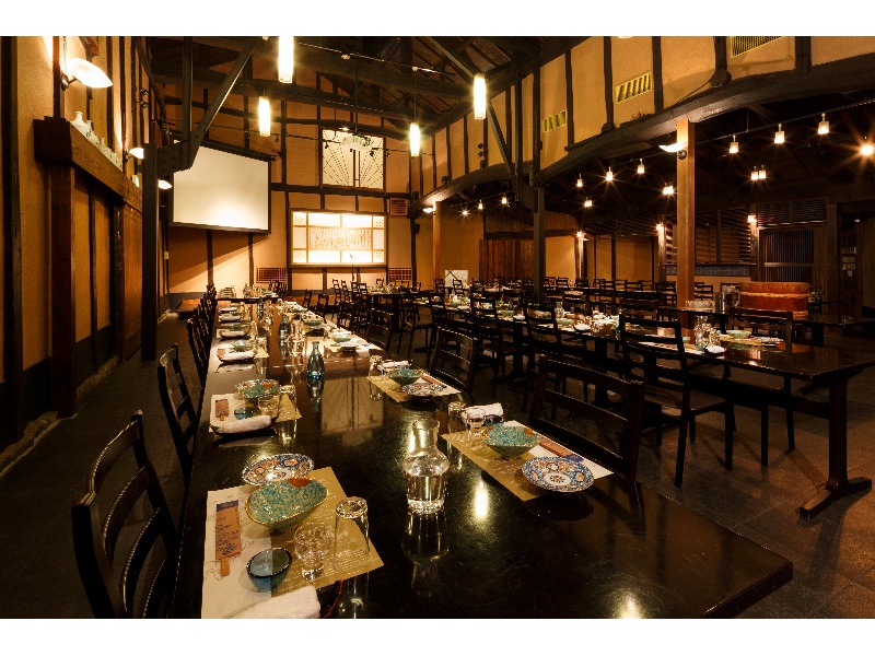 【百年蔵ホール】着席最大100名様。着席・立食などレイアウト変更対応可。プロジェクター・スクリーン・マイク・音響設備完備。土壁に黒を基調としたインテリアが映えるモダンな空間です。